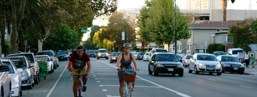 Happy bike riders making their way down an extra wide bike lane on a verdant street.